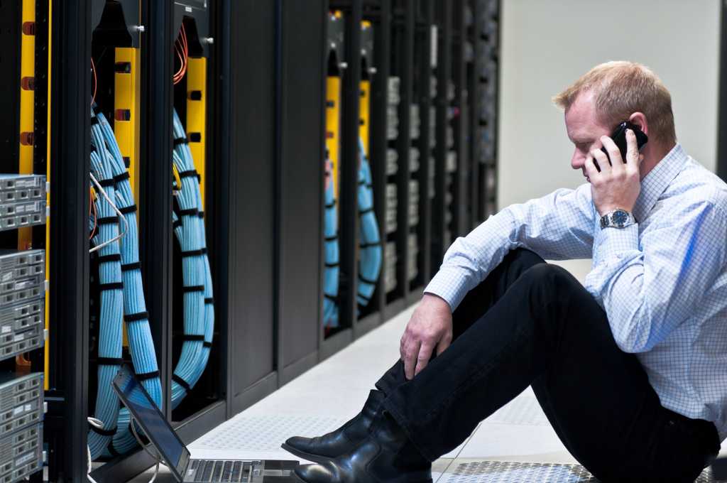 business man calling on a smartphone and looking at a laptop computer in a network data center